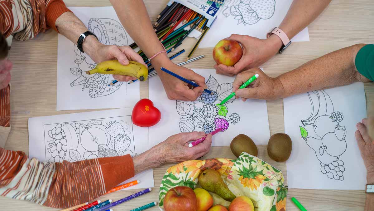 A carer and two senior citizens paint pictures together in the day care centre