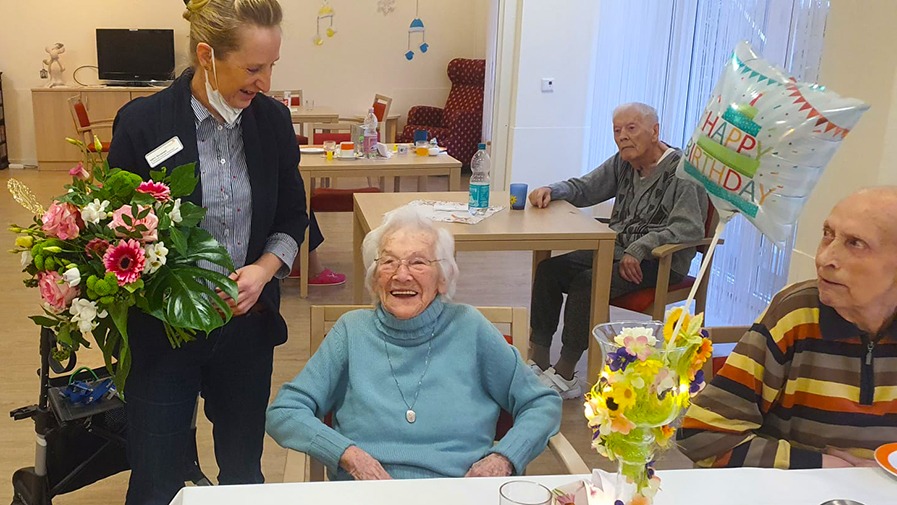 Einrichtungsleitung überreicht Seniorin zum 100-jährigen Geburtstag einen Blumenstrauß im Seniorenstift Neuenhagen-Hauptstraße