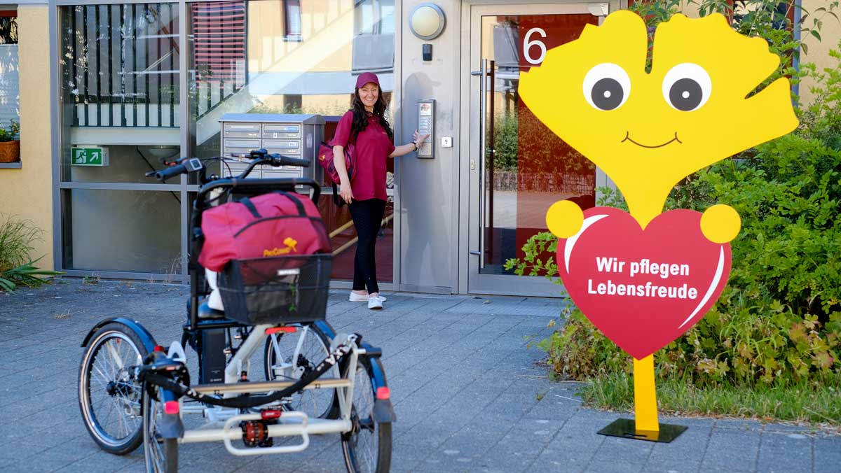 Pflegehelferin mit einem Vierrad und Ginkgo am Seiteneingang der Ambulanten Pflege Potsdam