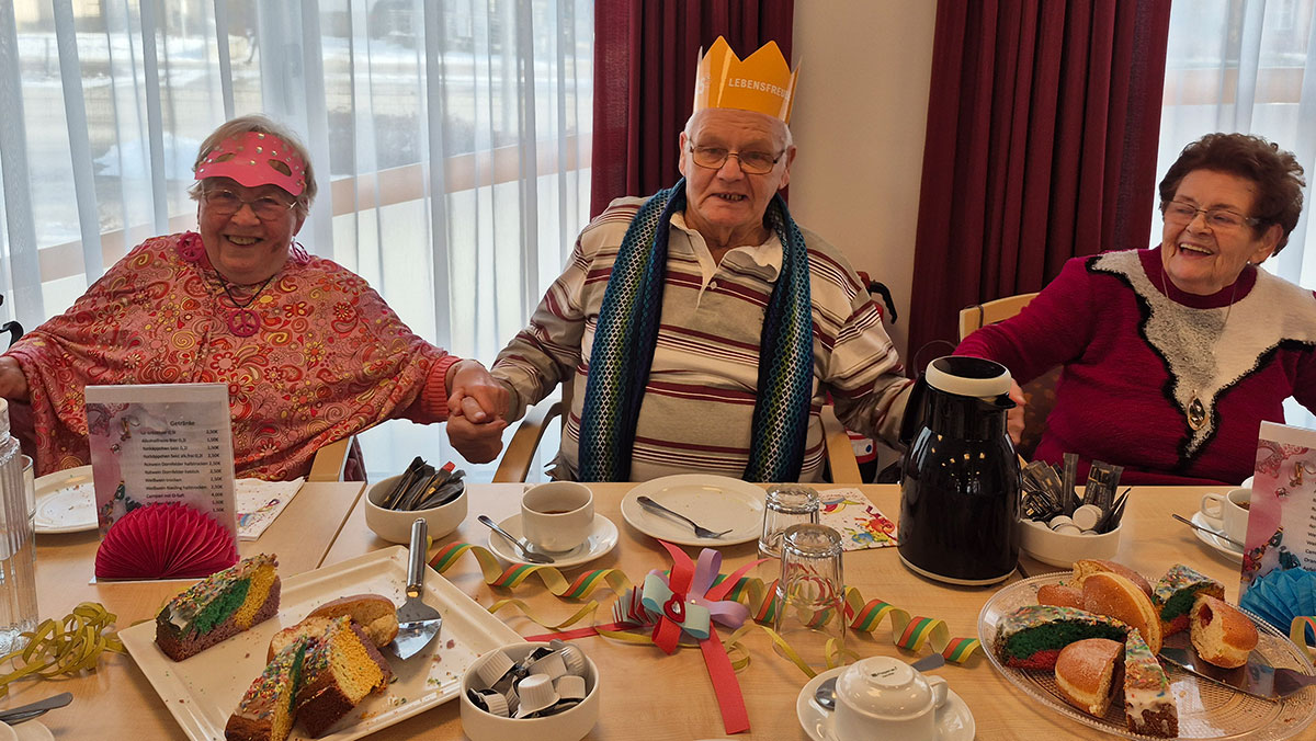 Faschingsfeier im ProCurand Service-Wohnen Wriezener Straße: Mieter*innen sitzen gemeinsam am Tisch, genießen Kuchen und Getränke und feiern gut gelaunt.